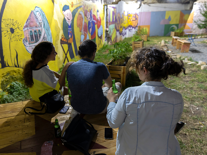 people sitting on a bench in laziza park with our illuminated graffiti wall in the background