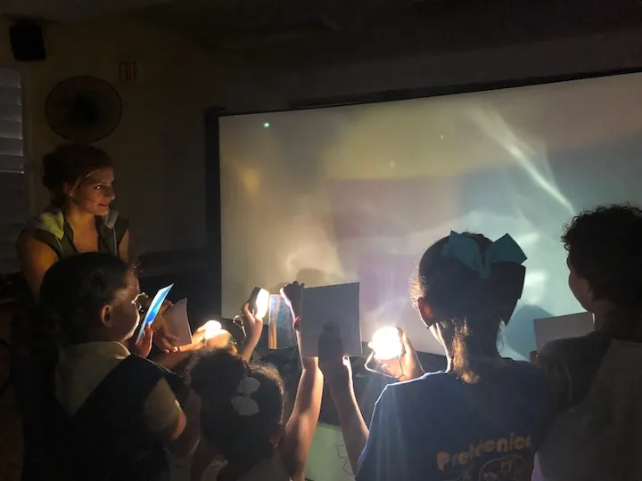 group of kids participating in a lighting workshop, learning to use portable lights with color filters to create new colors and shadows